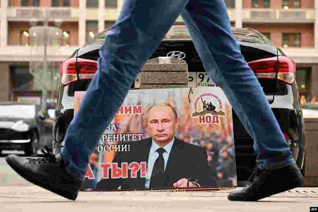 A placard featuring an image of Russian President Vladimir Putin and reading "We are with him for the sovereignty of Russia! And you?" is seen left in front of the Russian State Duma building in central Moscow.