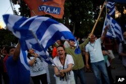 A supporter of the No vote waves a Greek flag after the referendum's exit polls at Syntagma square in Athens, Sunday, July 5, 2015.