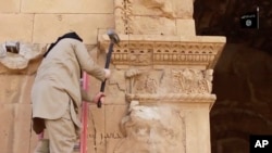 Seorang militan merusak patung berbentuk wajah manusia di dinding di kota kuno Hatra, Irak. (Foto: AP)