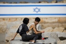People sit along the promenade as Israel rescinds the mandatory wearing of face masks outdoors in the latest return to relative normality, in Jaffa, Israel, April 18, 2021.