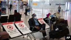 Seorang pria duduk sambil mengenakan pelindung wajah di Bandara Heathrow, London, Juli 2020.