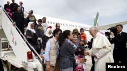 Paus Fransiskus menyambut sekelompok pengungsi Suriah setelah mendarat di bandar udara Ciampino di Roma setelah mengunjungi kamp pengungsi Moria di pulau Lesbos, Yunani (16/4). (Reuters/Filippo Monteforte)