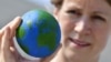 FILE - An environmental militant shows an orange, painted as a globe, during an event to mark the Earth Overshoot Day on Aug. 1, 2018 in Berlin. It marks the date when we (all of humanity) have used more from nature than our planet can renew in the entire year.