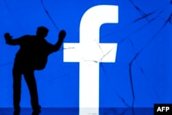 This photograph taken on May 16, 2018, shows a figurine standing in front of the logo of social network Facebook on a cracked screen of a smartphone in Paris.