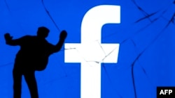 This photograph taken on May 16, 2018, shows a figurine standing in front of the logo of social network Facebook on a cracked screen of a smartphone in Paris. 