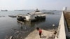 Orang-orang berjalan di dekat tanggul laut raksasa yang digunakan sebagai pembatas untuk mencegah air laut mengalir ke daratan dan menyebabkan banjir di Jakarta, 27 Juli 2019. (Achmad Ibrahim/AP)
