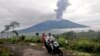 Ljudi prolaze vozeći se na motociklu dok vuklan Marapi izbacuje vulkanski material u Agamu, zapadna Sumatra, Indonezija, 4. decembra 2023.