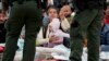 Una mujer sostiene su pulsera para mostrar a los agentes de la Patrulla Fronteriza de EEUU que ella y su hija han estado esperando más tiempo entre dos muros fronterizos para solicitar asilo, el viernes 12 de mayo de 2023, en San Diego. (Foto AP/Gregory Bull)