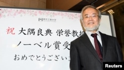 Yoshinori Ohsumi, guru besar di Institut Teknologi Tokyo, Jepang, tersenyum di depan papan ucapan selamat atas perolehan anugerah Nobel Kedokteran 2016 di Yokohama, 3 Oktober 2016 (Foto: Kyodo). 