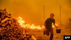 Alex Schenck carries a water bucket while fighting to save his home as the Ranch Fire tears down New Long Valley Rd near Clearlake Oaks, California, on Saturday, August 4, 2018.