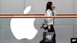在北京一个购物中心，一名女子提着美国服装品牌Abercrombie & Fitch的购物袋走过苹果商店（2019年2月26日）