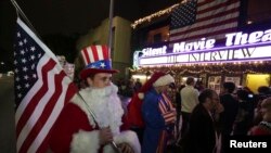 Matt Ornstein, mengenakan kostum Sinterklas, memegang bendera Amerika saat para pengunjung antri membeli tiket untuk menonton pemutaran perdana film "The Interview" di Los Angeles, California (24/12).