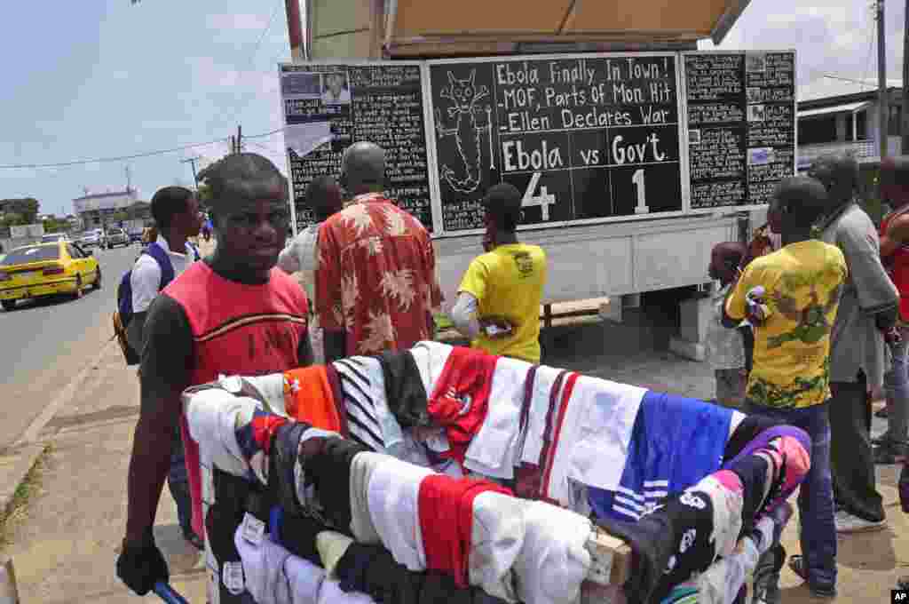 A man sells clothes as he walks past people reading comments on a blackboard that informs the public of current events in Liberia, including information on the Ebola virus, in Monrovia, Liberia, Saturday Aug. 2, 2014. 