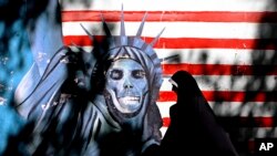 FILE - An Iranian woman walks past graffiti art characterizing the U.S. Statue of Liberty, painted on the wall of the former US embassy in Tehran, Iran, Sept. 25, 2007. 