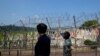 Visitors wearing face masks as a precaution against the coronavirus, walk near the barbed-wire fences decorated with ribbons written with messages wishing for the reunification of the two Koreas at the Imjingak Pavilion in Paju, South Korea,…