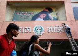 Seorang penonton bioskop memotret petugas yang memasang poster film Bollywood di luar Teater Maratha Mandir di Mumbai, 12 Desember 2014.