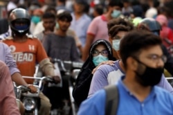 seorang wanita mengendarai sepeda motor saat dia mengenakan masker pelindung di tengah serbuan orang di luar pasar ketika wabah penyakit coronavirus (COVID-19) berlanjut, di Karachi, Pakistan 8 Juni 2020