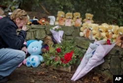 FILE - Cheryl Girardi, of Middletown, Conn., kneels beside 26 teddy bears, each representing a victim of the Sandy Hook Elementary School shooting, at a sidewalk memorial, Dec. 16, 2012, in Newtown, Conn.