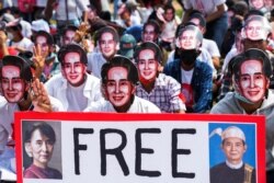 Protesters wearing masks depicting ousted leader Aung San Suu Kyi, flash three-finger salutes as they take part in a protest against the military coup in Yangon, Myanmar, February 28, 2021.