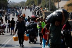 FILE - Migrants carry their belongings as they flee a road leading from Moria to the capital of Mytilene, on the northeastern island of Lesbos, Greece, Sept. 17, 2020.