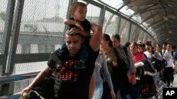 Para migran asal Kuba dikawal oleh para pegawai imigrasi di Ciudad Juarez, Meksiko, saat mereka menyeberangi jembatan internasional Paso del Norte untuk diproses sebagai pencari suaka di sisi perbatasan wilayah AS, 29 April 2019.
