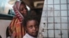 Seorang ibu dan anak perempuannya tengah menunggu bus di Izba, dekat Khartoum, Sudan, 14 Apri 2015. (Foto: dok).