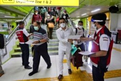 Para petugas membagikan imbauan kesehatan kepada penumpang kereta saat diberlakukannya PSBB di tengah pandemi di Stasiun Gambir di Jakarta, 28 Mei 2020. (Foto AP).