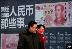 FILE - A couple walk past a display showing the security features of the new 100 Yuan note in Beijing, Monday, Jan. 11, 2016.