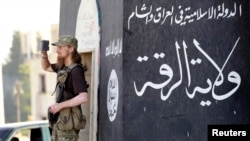 FILE - A militant Islamist fighter uses a mobile device to film his fellow fighters taking part in a military parade along the streets of Syria's northern Raqqa province.