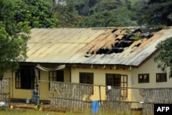 FILE - A woman stands outside the damaged roof of a school's dormitory, after it was set on fire, in Bafut, in the northwest English-speaking region of Cameroon, Nov. 15, 2017.