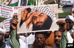 FILE - Indian Muslims hold a scratched photo of Jaish-e-Mohammad group chief, Maulana Masood Azhar, as they shout slogans against Pakistan during a protest in Mumbai on Feb. 15, 2019.