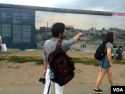 A Syrian refugee at the Berlin Wall looks at a photo gallery of the destruction of his country by war, June 30, 2016. Young Syrian men say they want to go home, but only after the war. (H. Murdock/VOA)