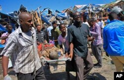 Somali men retrieve the dead body of a person who was killed when a car bomb targeted a police station in the Waberi neighborhood, where President Hassan Sheikh Mohamud was visiting a university, in the capital Mogadishu, Saturday, Nov. 26, 2016.