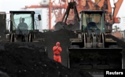 FILE - An employee walks between front-end loaders which are used to move coal imported from North Korea at Dandong port in the Chinese border city of Dandong, Dec. 7, 2010.
