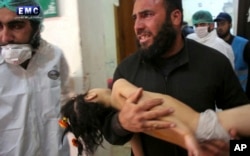 FILE - This April 4, 2017, photo provided by the Syrian anti-government activist group Edlib Media Center shows a man carrying a child following a suspected chemical attack at a makeshift hospital in the town of Khan Sheikhoun, Idlib province, Syria.