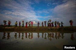 FILE - Rohingya refugees are reflected in rain water along an embankment next to paddy fields after fleeing from Myanmar into Palang Khali, near Cox's Bazar, Bangladesh, Nov. 2, 2017.