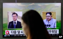 A woman walks past a TV screen showing file footage of South Korean President Moon Jae-in, left, and North Korean leader Kim Jong Un, right, during a news program shown at the Seoul Railway Station in Seoul, South Korea, March 29, 2018.
