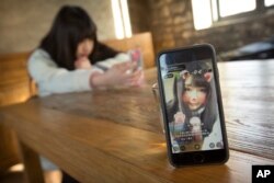 FILE - A smartphone shows online web performer Wang Weiying, 18, as she broadcasts a live stream from her smartphone in a cafe in Beijing.