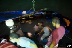 FILE - Rescuers work to help survivors and remove bodies of migrants trapped beneath the deck of a boat after it sank in the Mediterranean Sea off the coast of in Zuwara, Libya, Aug. 27, 2015.