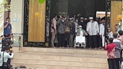 Abu Bakar Baasyir ( tengah-duduk berkursi roda- baju putih) melambaikan tangan di hadapan para jurnalis dan masyarakat yang berada di pintu gerbang Ponpes Ngruki, Sukoharjo , Jumat (8/1). (Foto: VOA/ Yudha Satriawan)