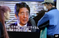 FILE - Passers-by look at a TV screen showing Japanese Prime Minister Shinzo Abe speak on North Korea's rocket launch, in Tokyo, Feb. 7, 2016.