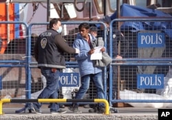 FILE-A masked Turkish police officer escorts a migrant after the first vessel transporting migrants from Greek island of Lesbos was docked in Dikili port, Turkey, putting into practice a European Union plan to stem migration to Europe, April 4, 2016.