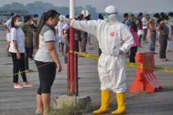 Seorang petugas kesehatan memeriksa suhu pekerja migran Indonesia yang tiba dari Malaysia selama karantina untuk mencegah penyebaran Covid-19, di pangkalan udara Soewondo di Medan, Sumatra Utara, 11 April 2020.