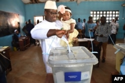 FILE - Sierra Leone's People Party presidential candidate Julius Mada Bio holds his daughter while casting his ballot for the general elections, at a polling station in Freetown, March 7, 2018, as his wife looks on.