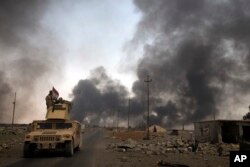 FILE - Iraqi security forces patrol as smoke rises from burning oil wells in Qayara, south of Mosul, Iraq, Aug. 31, 2016.