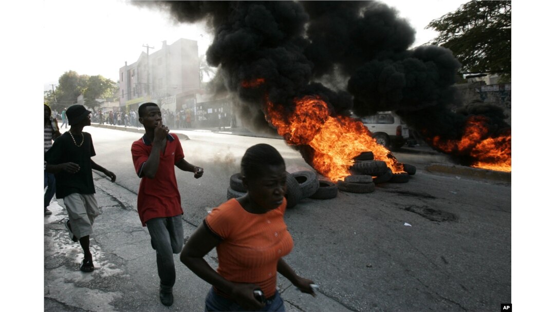 FILE - Local residents run past burning tires outside the Delmas police station in Port-au-Prince, Dec 20, 2006. Riots erupted after residents surrounded the police station throwing stones and bottles demanding that the police hand over two suspected kidnappers to lynch them.
