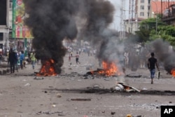 FILE - People walk near burning debris during election protests in Kinshasa, Democratic Republic of Congo, Sept. 19, 2016.