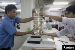 A staff hands a stack of Myanmar Kyat to another at a bank in Yangon October 19, 2015. To match Insight MYANMAR-DOLLARS/ REUTERS/Minzayar - GF10000251135