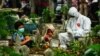 Seorang anggota keluarga mengenakan pakaian pelindung diri (APD) bersama dua anak berdoa di dekat makam korban COVID-19 yang baru saja dimakamkan, di Lhokseumawe, Aceh, 18 Mei 2021. (Azwar Ipank / AFP)