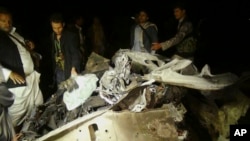 FILE - Shi'ite Houthi rebels stand next to a wreckage of a vehicle at the site of a car bomb attack in Sana'a, Yemen, June 17, 2015.